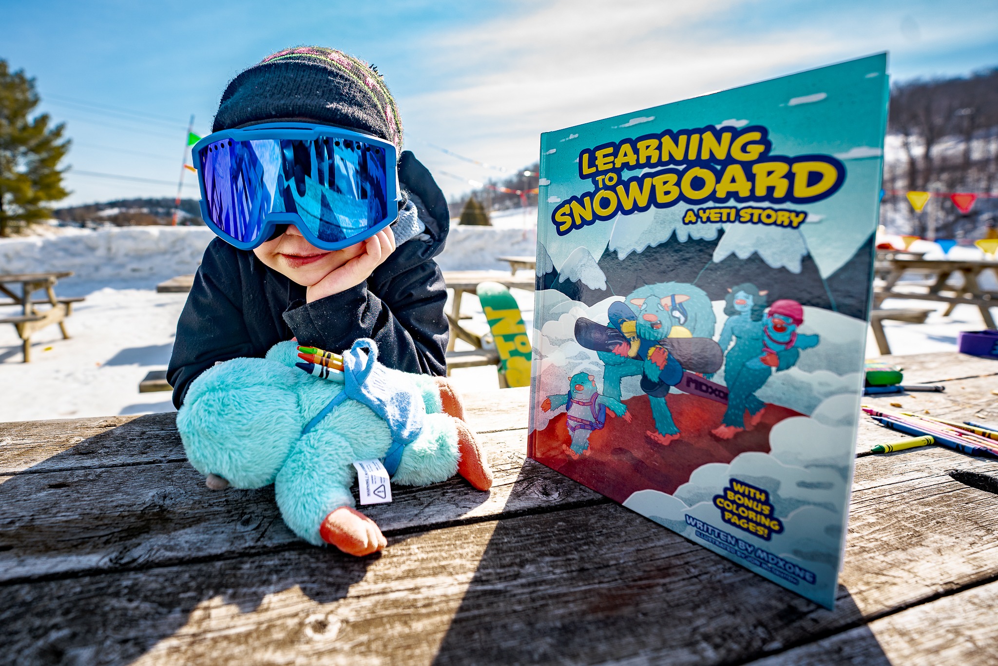 Child at a snowy picnic table with a Yeti plush and Learning to Snowboard: A Yeti Story book