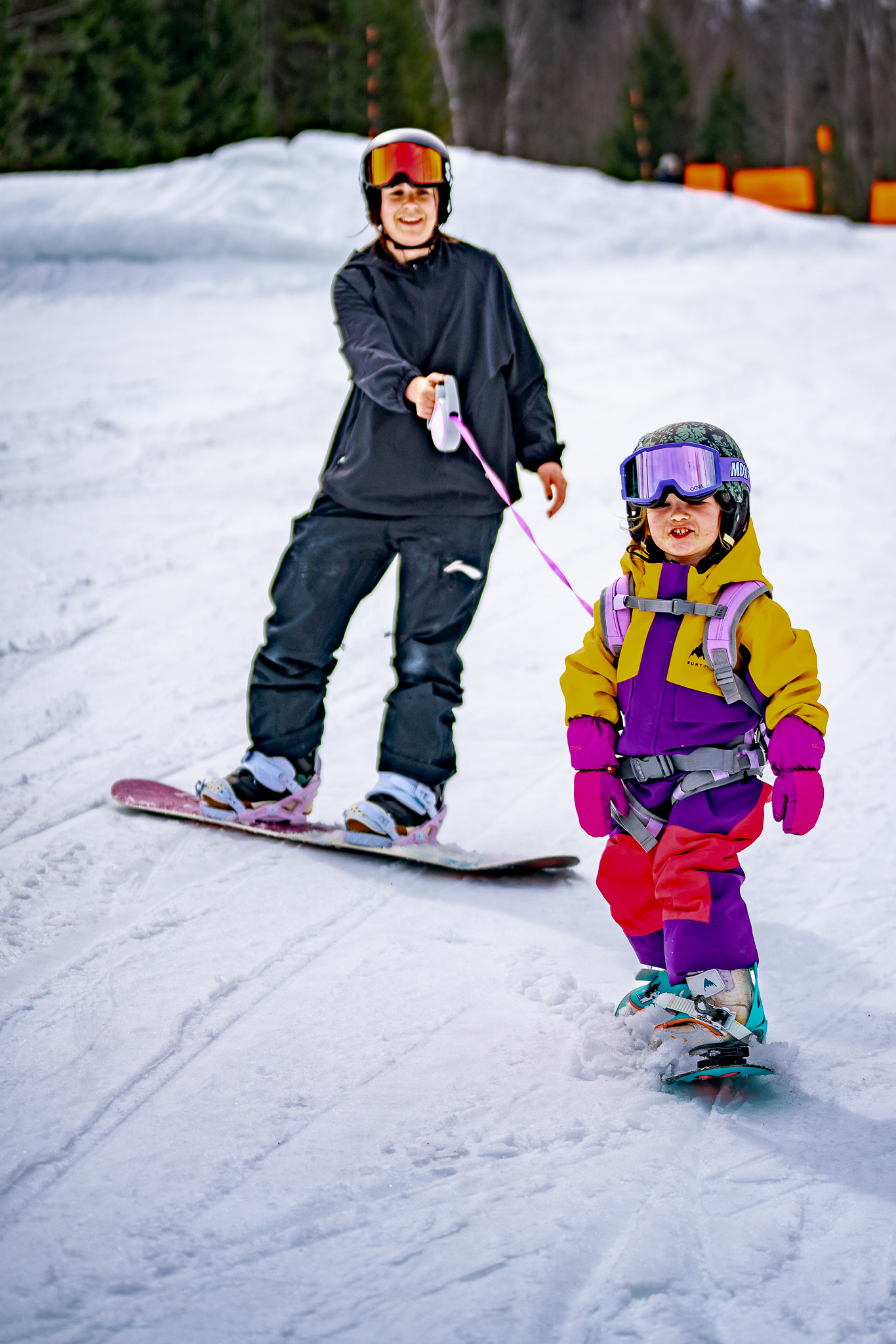 Little girl and her mom snowboarding together with the MDXONE retractable teaching leash