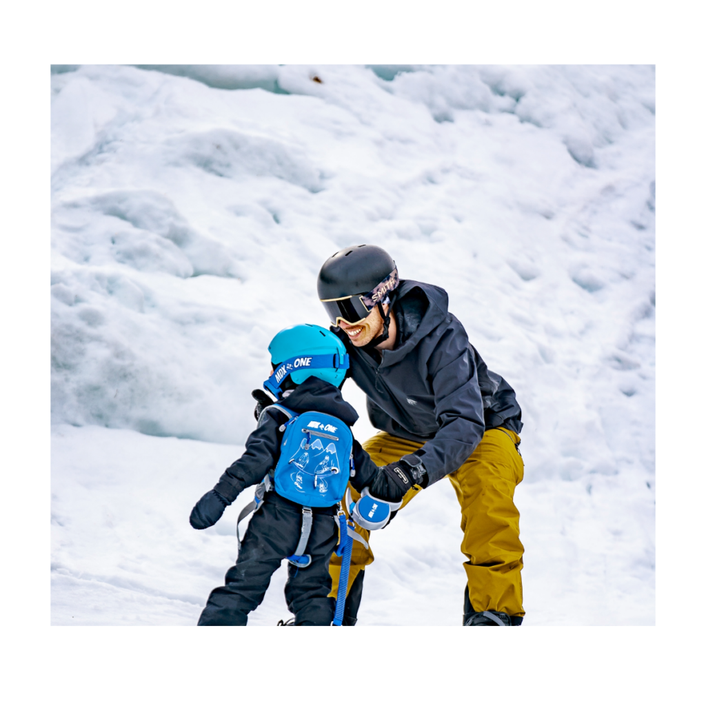 Parent helping a child wearing the Blue THEONE backpack harness on snow
